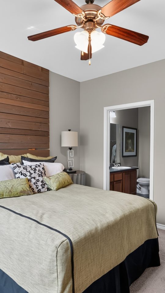 Bright Outlook Ridge Apartments bedroom with a queen bed, wood accent wall, ceiling fan, plush carpet, and private bath access.