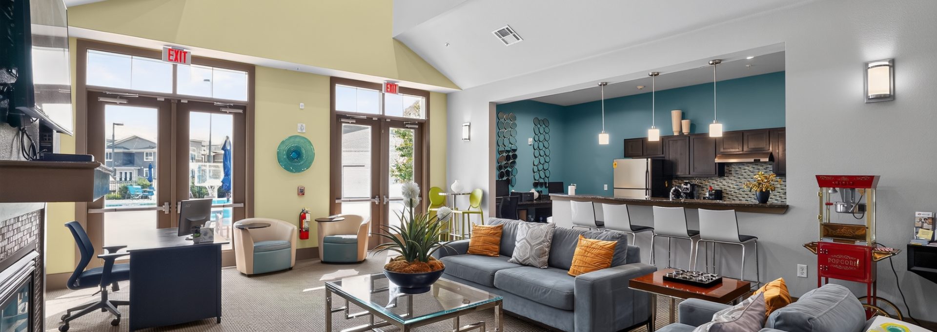 Upscale apartment community lounge with kitchen, couches, and desk. Views of a pool outside.
