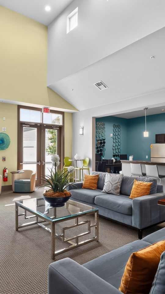 Upscale apartment community lounge with kitchen, couches, and desk. Views of a pool outside.