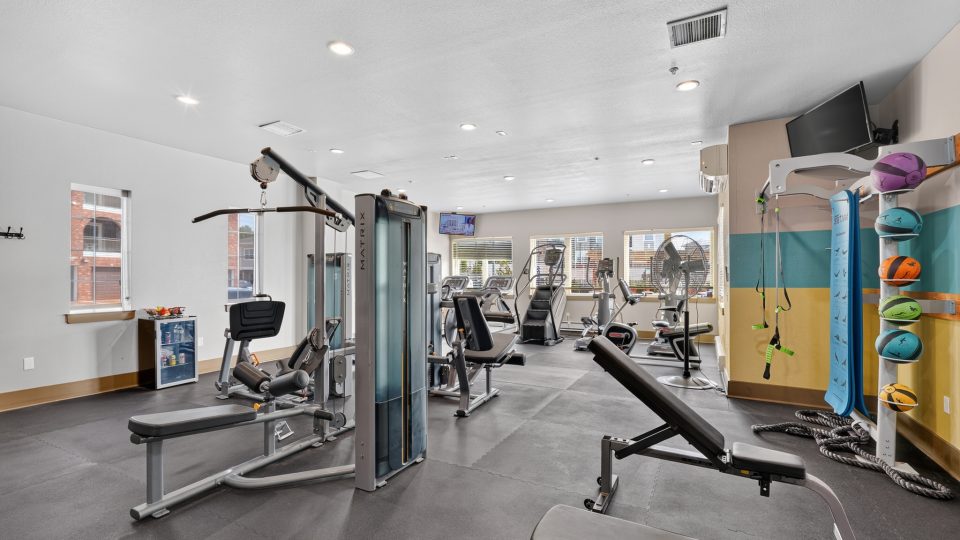 Apartment complex gym featuring cardio, weight, and strength machines. Includes TVs and a refreshment fridge for residents.