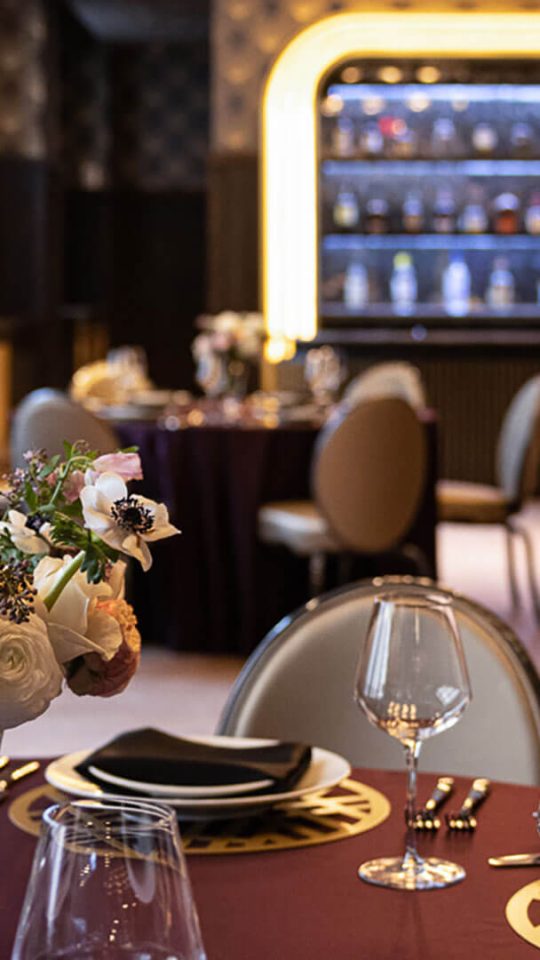 a restaurant setting with purple table cloths and wine glasses at The First