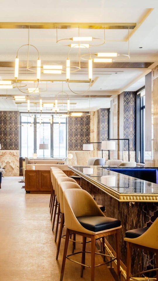 the lobby of a hotel with a long bar and chairs at The First