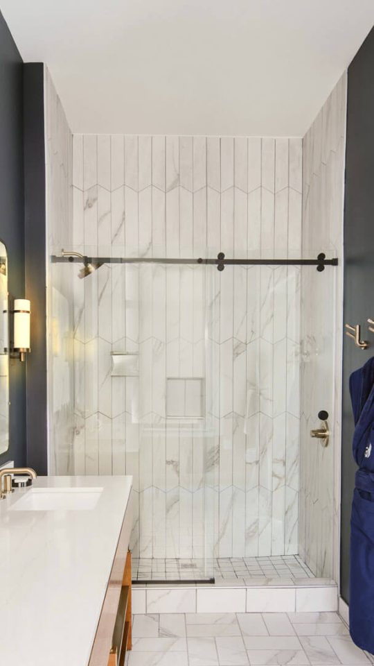 a bathroom with a marble counter top and a glass shower door at The First