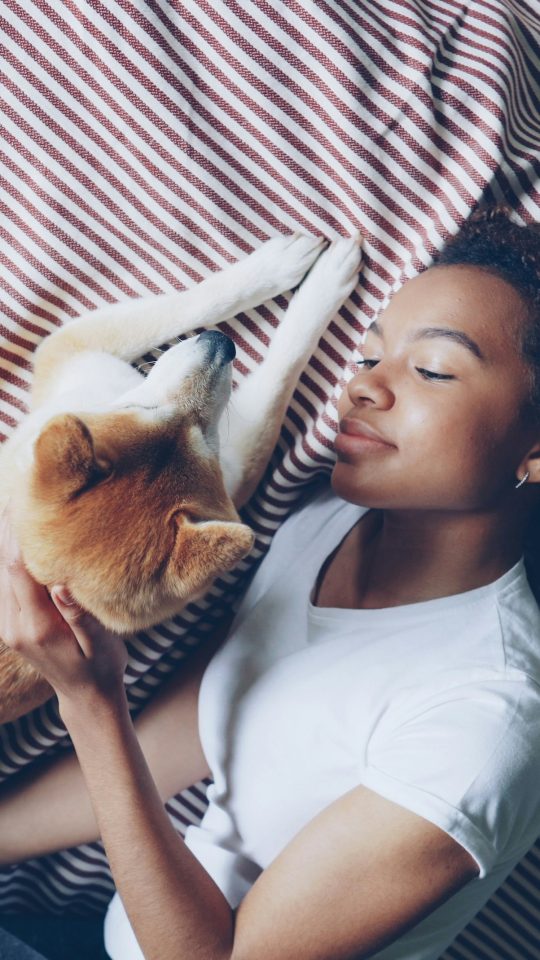 A woman lays with her dog on a bed.