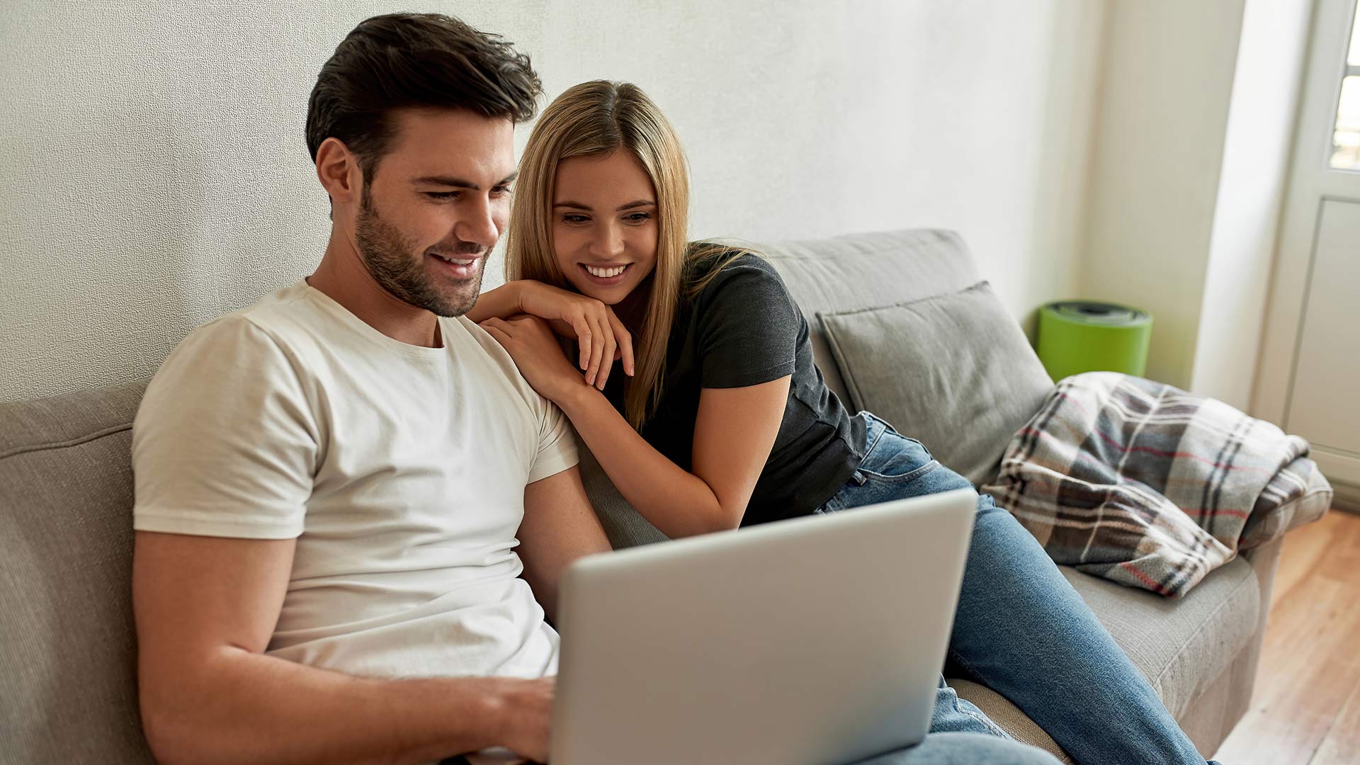 a man and woman are sitting on a couch and looking at a laptop at The Cedars Apartments