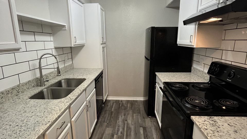 a kitchen with white cabinets and black appliances at The Cedars Apartments