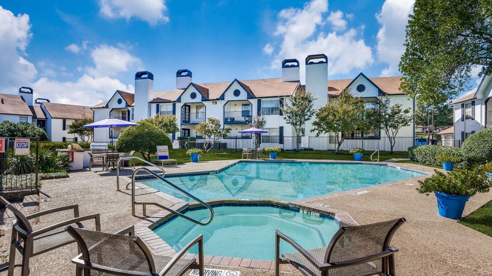 Pool and Hot Tub surrounde by green area and seating, as well as a grill under a parasol