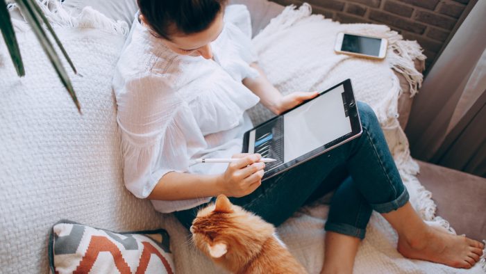 woman sitting on the couch with a cat and a tablet at The Breezeway Townhomes