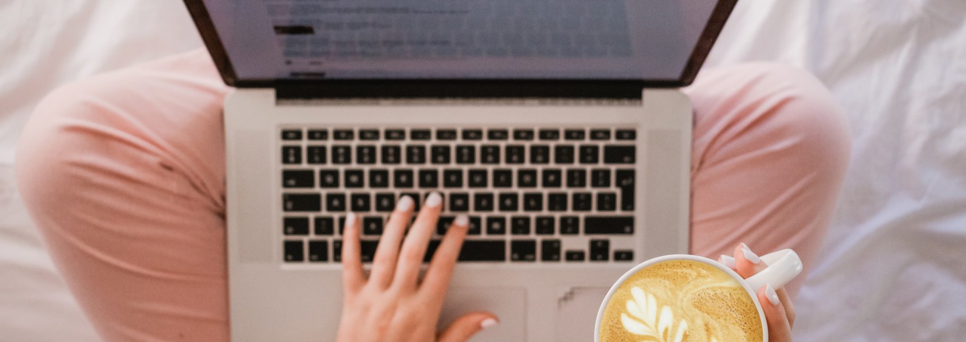 person using MacBook Pro and holding cappuccino