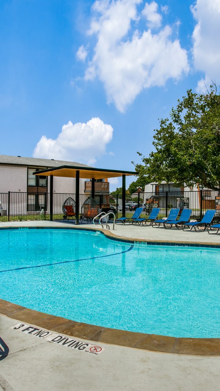 Swimming pool with blue lounge chairs at 8500 Harwood apartments in North Richland Hills, Texas