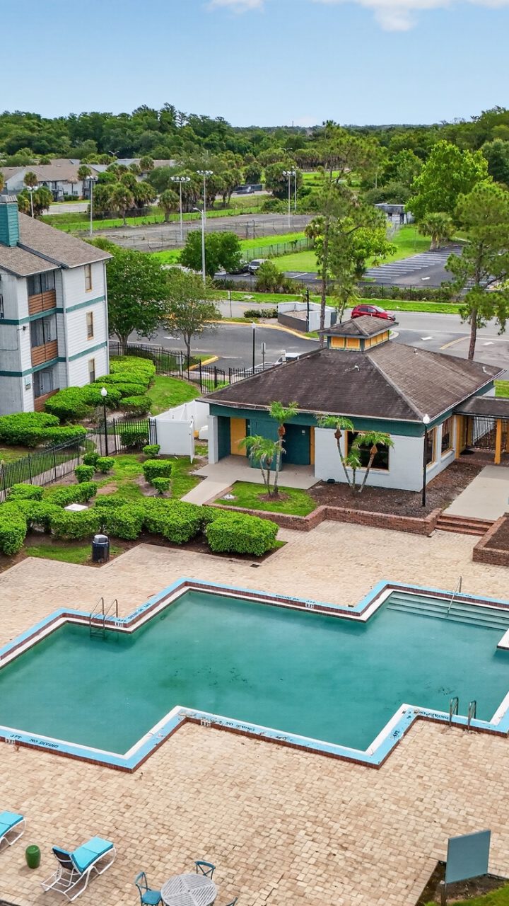 Aerial view of the swimming pool, blue loungers and landscaped buildings at Lorenzo at East Mil Apartments in Orlando, Florida