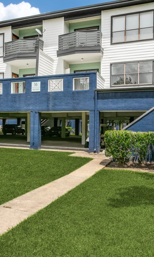 the front of an apartment building with grass and trees at The Pearce on  Lake