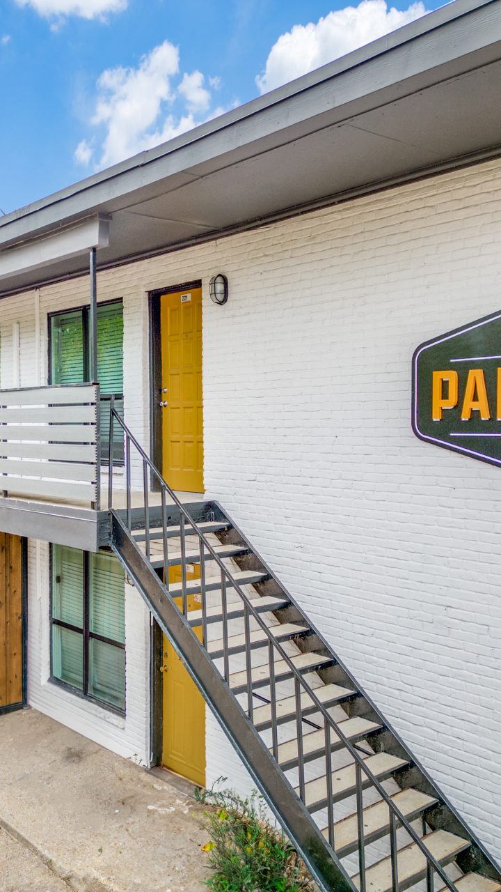 Palmilla Apartments building with white brick walls, yellow doors and community sign in Irving, Texas