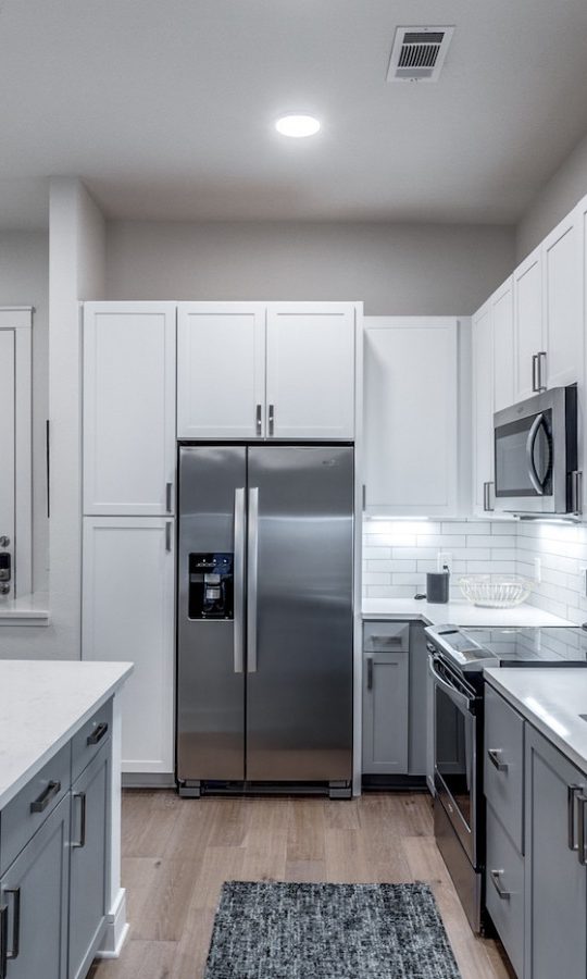 a clean kitchen with stainless steel appliances and white cabinets at The Teak at  Branch