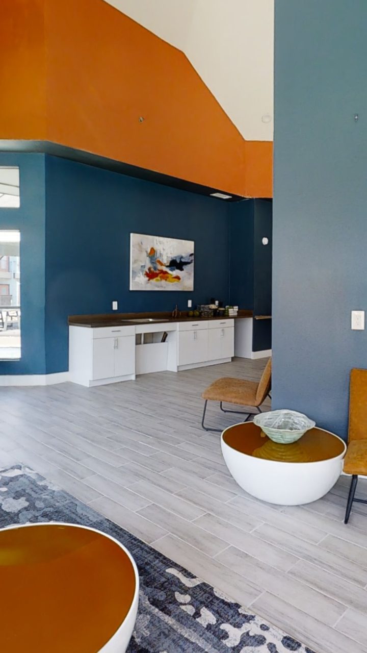 Sunlit clubhouse lounge with blue walls, orange accents and pool views at Felix Apartments in Arlington, Texas