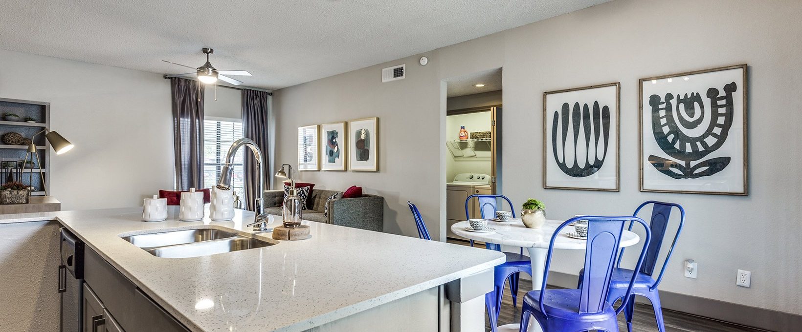 a kitchen with a sink, counter top and blue chairs at The Hyde Park at Valley Ranch