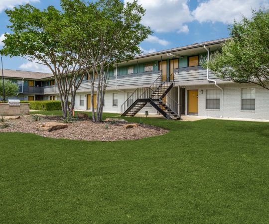 the exterior of an apartment complex with lawn and trees at The Las Ventanas