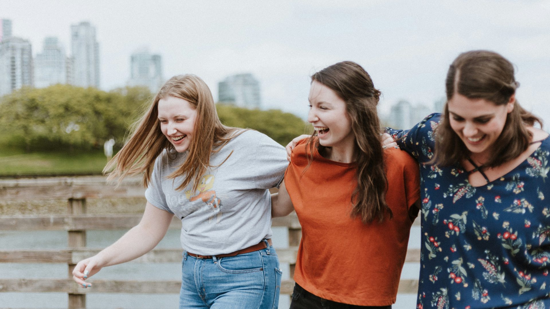 three women walking on brown wooden dock near high rise building during daytime